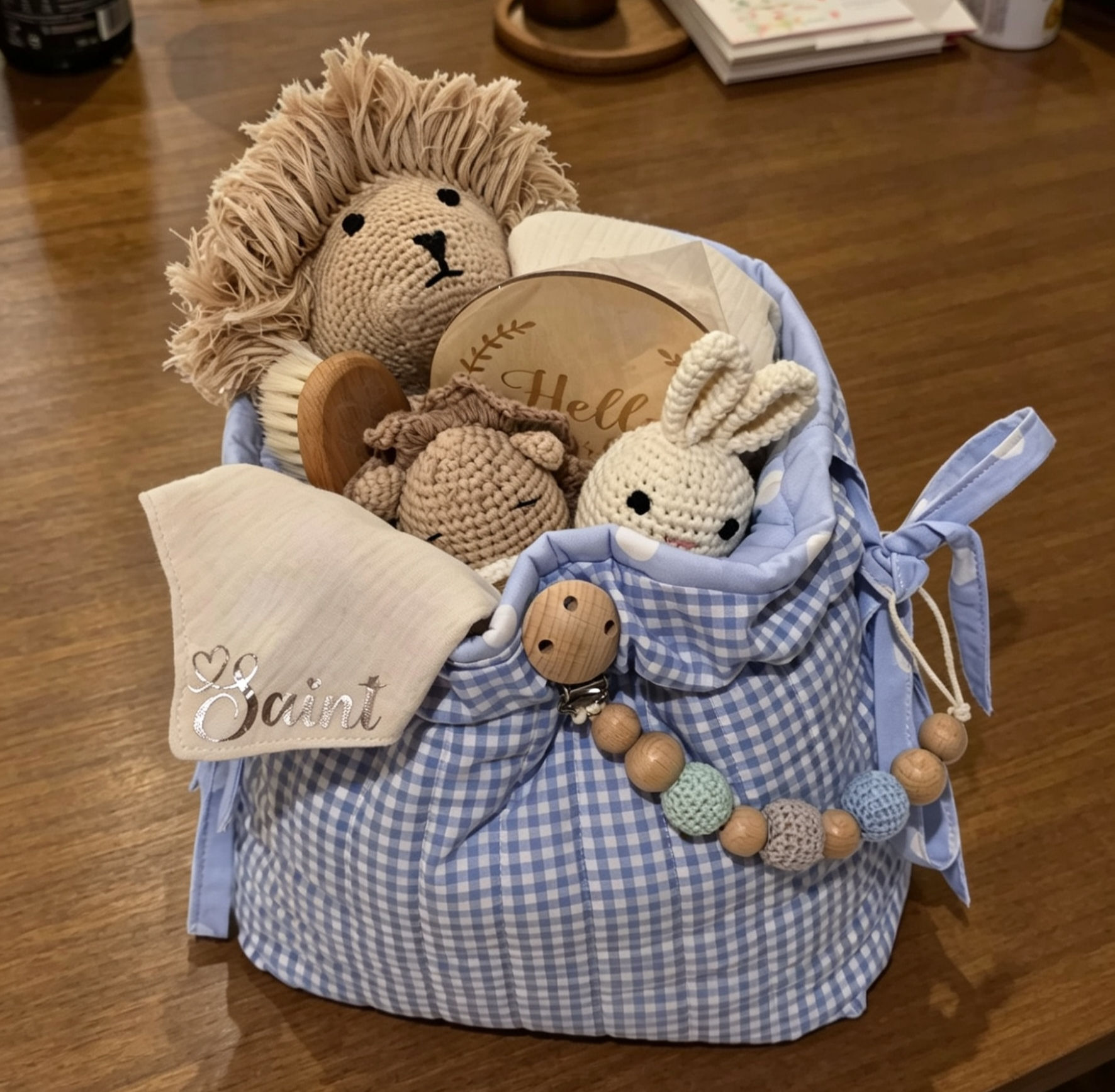 Personalised baby gift hamper with crochet lion and bunny toys, embroidered muslin cloth, wooden milestone disc and beaded dummy clip in a blue gingham basket